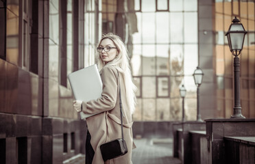 Stylish blonde business woman with laptop in trench coat in urban location