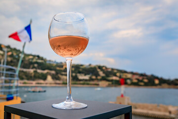 Glass of rose wine with Mediterranean Sea and French tricolor flag in background, Villefranche sur Mer Old Town on the French Riviera, South of France