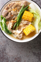 beef shank soup with marrow bones, corn cobs, napa cabbage, onion, bok choy closeup in the bowl on the table. Vertical top view from above