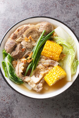 Beef Bulalo is a popular Filipino beef soup with vegetables such as Napa cabbage, green onion, bok choy and corn closeup in the bowl on the table. Vertical top view from above