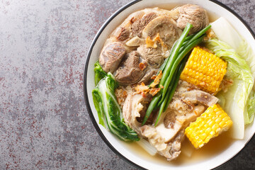 Bulalo is a Filipino boiled soup made with bone-in beef shanks, corn and cabbage leaves closeup in the bowl on the table. Horizontal top view from above