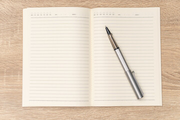 Rollerball pen is placed on the blank notebook. The notebook have lines and day boxes and subject. It seems someone is going to write the journall, diary, planner or to-do list.   © MU Studio