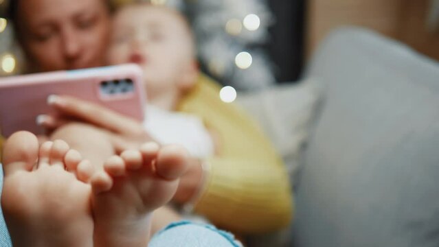 Close-up shot of baby's feet on mom's lap enjoying looking at the phone at home