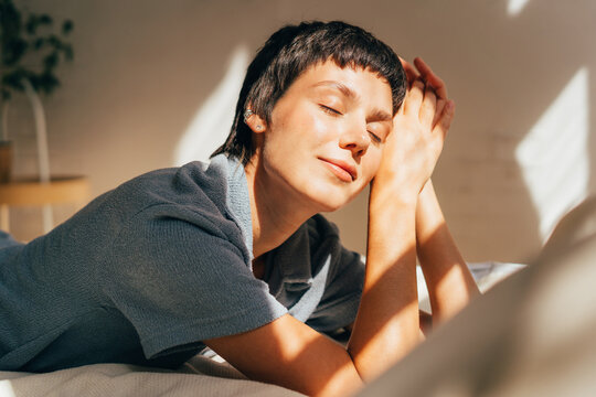 A woman lies on a bed in bright sunlight from the window.