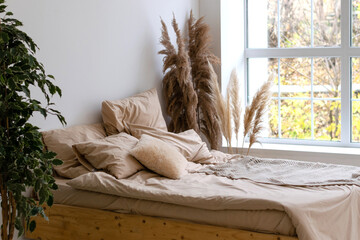 Bedroom interior.A bed with beige linens, a bouquet of pampas grass, a large window.Eco-friendly...