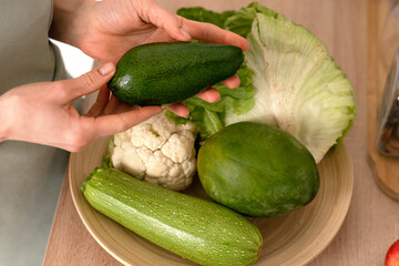 Avacado,cauliflower,mango,zucchini on a plate on the kitchen table,female hands close up.Healthy eating and healthy lifestyle.Cooking at home.Veganuary,vegetarian and vegan diet.Selective fosus.