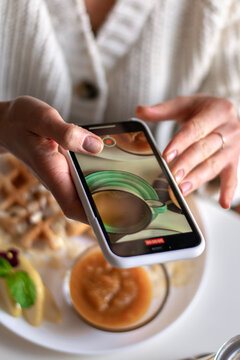 A woman taking picture of her food on the smartphone in a vegan cafe before eating.Hands close-up, top view, selective focus.