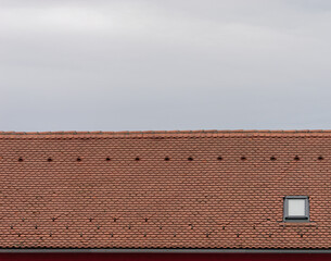 Close-up photo of a red roof tile with one window  and a bright sky in the background