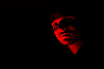 Portrait face of a young Indian guy, with red color light in the dark.