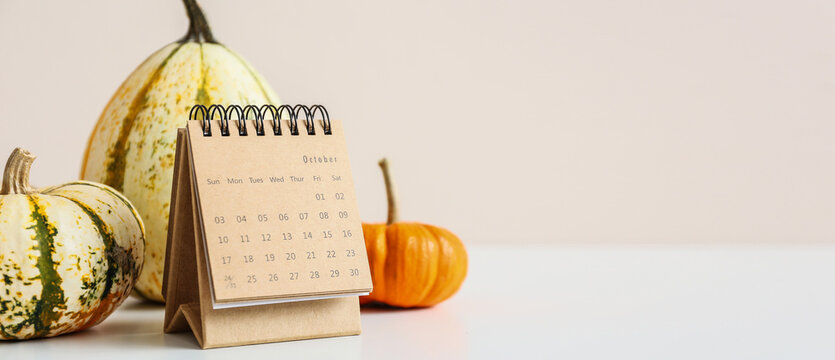 Calendar with open page of October month and pumpkins on light background with space for text