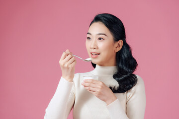 Young female enjoying taste of yogurt isolated on pink