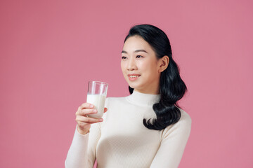 Portrait of a satisfied young asian woman drinking milk from the glass isolated over pink background