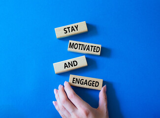 Stay Motivated and Engaged symbol. Concept words Stay Motivated and Engaged on wooden blocks. Beautiful blue background. Businessman hand. Business and Stay Motivated and Engaged concept. Copy space