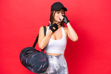 Young beautiful sport woman with sport bag isolated on red background is suffering with cough and feeling bad