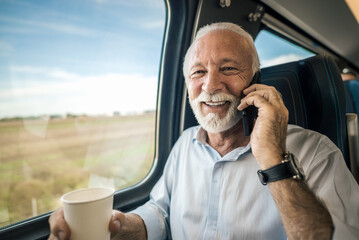 Smiling businessman entrepreneur professional talking on smart phone while having coffee on intercity train.