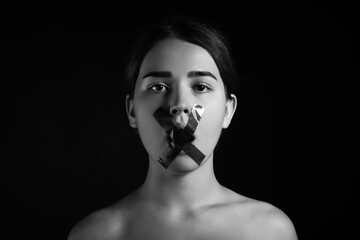 Young woman with taped mouth on dark background. Censorship concept