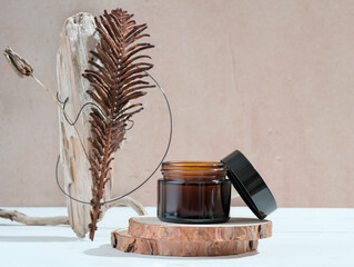 Cometic glass jar for cream and dry plants and driftwood on a pastel beige background. Skin care products packaging design. Spa concept. modern trendy style