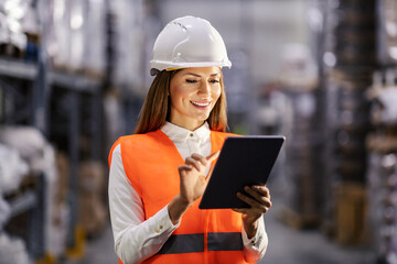 A happy storage manager is using tablet in facility and smiling at it.
