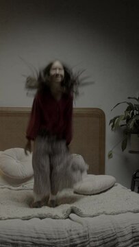 young asian girl, long dark hair bouncing jumping on bed, star jumps
