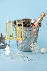Glasses of champagne, ice bucket with bottle and Christmas decorations on color background