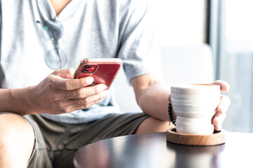 man playing red smartphone holding coffee cup
