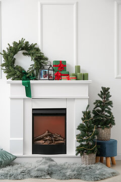 Fireplace with presents, decor and Christmas trees near light wall