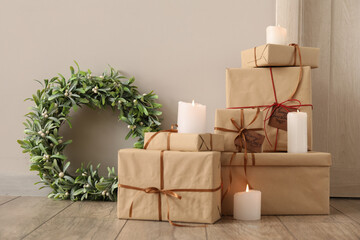 Christmas mistletoe wreath, presents and candles near light wall