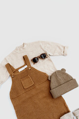 Knitted jumpsuit, sweater, warm hat, sunglasses on white background. Set of baby fashion clothes and accessories