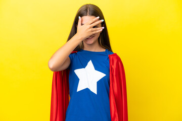 Little caucasian superhero girl isolated on yellow background covering eyes by hands and smiling © luismolinero
