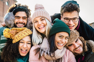 International guys and girls taking funny selfie on warm fashion clothes - Happy life style concept with millenial people having fun together out side on winter holidays - Bright warm filter
