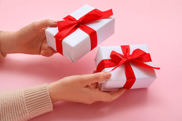 Female hands with Christmas gifts on pink background, closeup