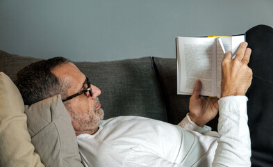 Obraz premium Middle age man with eye glasses reading book at home on couch.