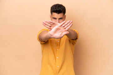 Young caucasian man isolated on beige background making stop gesture with her hand to stop an act - Powered by Adobe