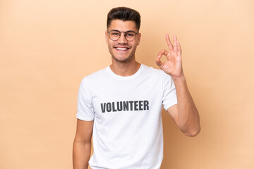 Young volunteer caucasian man isolated on beige background showing ok sign with fingers