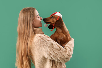 Young woman with dachshund dog in Santa hat on green background