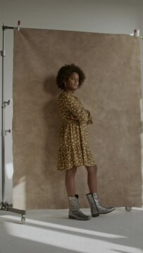 Young black girl with afro standing in front of a backdrop in photography studio looking confident