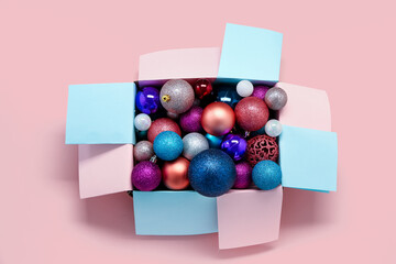 Box with different Christmas decorations on pink background