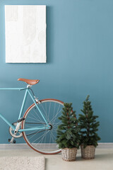 Bicycle and small fir trees near blue wall in room