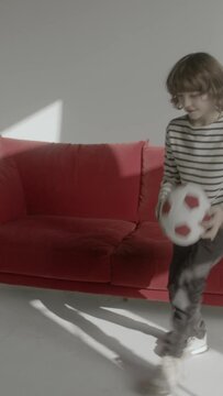 a young boy playing with a football next to a red sofa in a white room