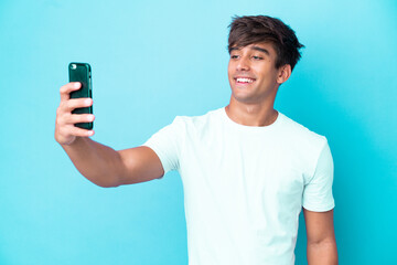 Young caucasian man isolated on blue background making a selfie with mobile phone