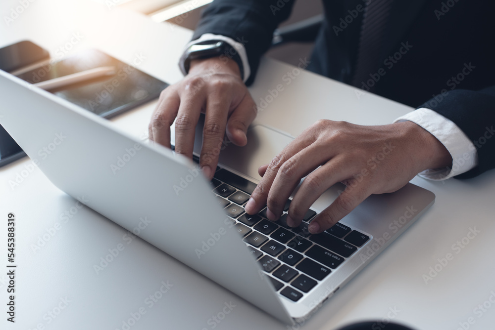 Wall mural Close up of businessman working with laptop computer on table at office. Business man hands typing on laptop, online working, surfing the internet