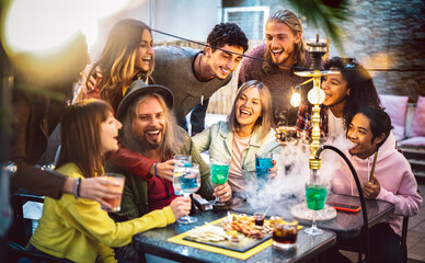 Happy friends having fun drinking cocktails at shisha bar - Mixed age range people toasting drinks...