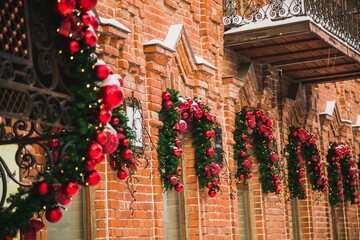 Fototapeta na wymiar Stylish christmas fir branches with red baubles and sparkling garland on front of door at holiday market or restaurant in city street. Winter christmas street decor