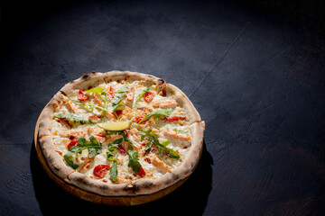 Pizza with salmon, mozzarella, cherry tomatoes, arugula, lemon and parmesan. Italian cuisine. On a black background. Free space for text. View from above.