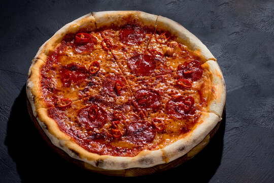 Pizza with tomato sauce, mozzarella, salami, chili, honey on black background. View from above
