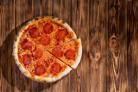 Pizza with tomato sauce, mozzarella, salami on wood background. View from above, copy space
