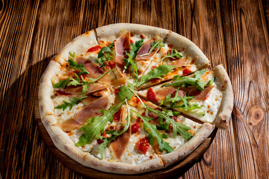 Pizza with jamon and prosciutto, mozzarella, cherry tomatoes, arugula and parmesan on a wood background. Italian cuisine.