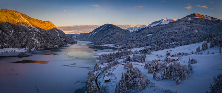 The beautiful setting of the Weissensee Nature Park. Frozen Lake Weissensee, Carinthia, Alps, Austria. Aerial drone shot in January 2022. Sunset time.