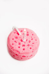 Burning white holiday candle on  pink sponge in the shape of cake. isolated