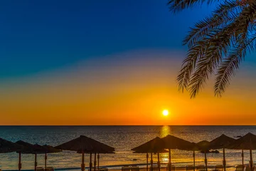 Rolgordijnen sonnenaufgang auf kreta mit strandschirm und palme © Andreas Nowack